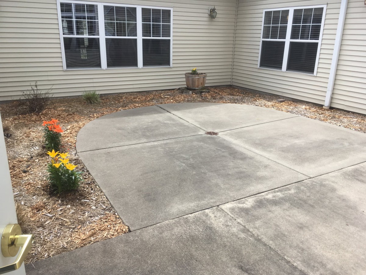 A concrete patio area with surrounding flower beds and windows on a building exterior.