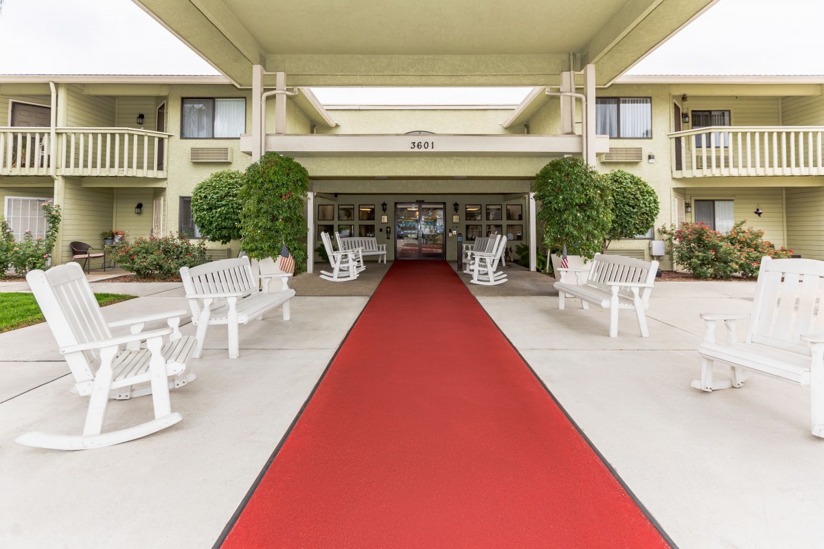 A red carpet leads to the entrance of a building, flanked by white benches and greenery.