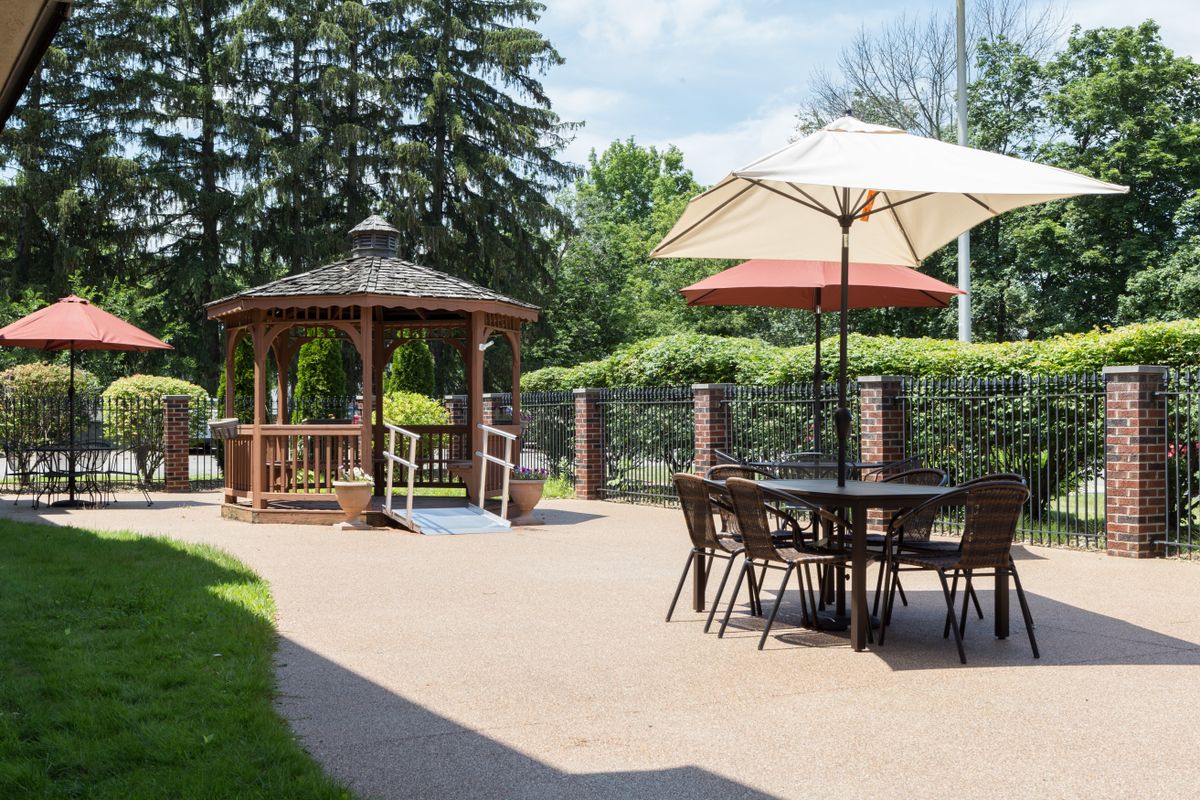 A tranquil outdoor patio featuring a wooden gazebo and seating area with umbrellas, surrounded by lush greenery.