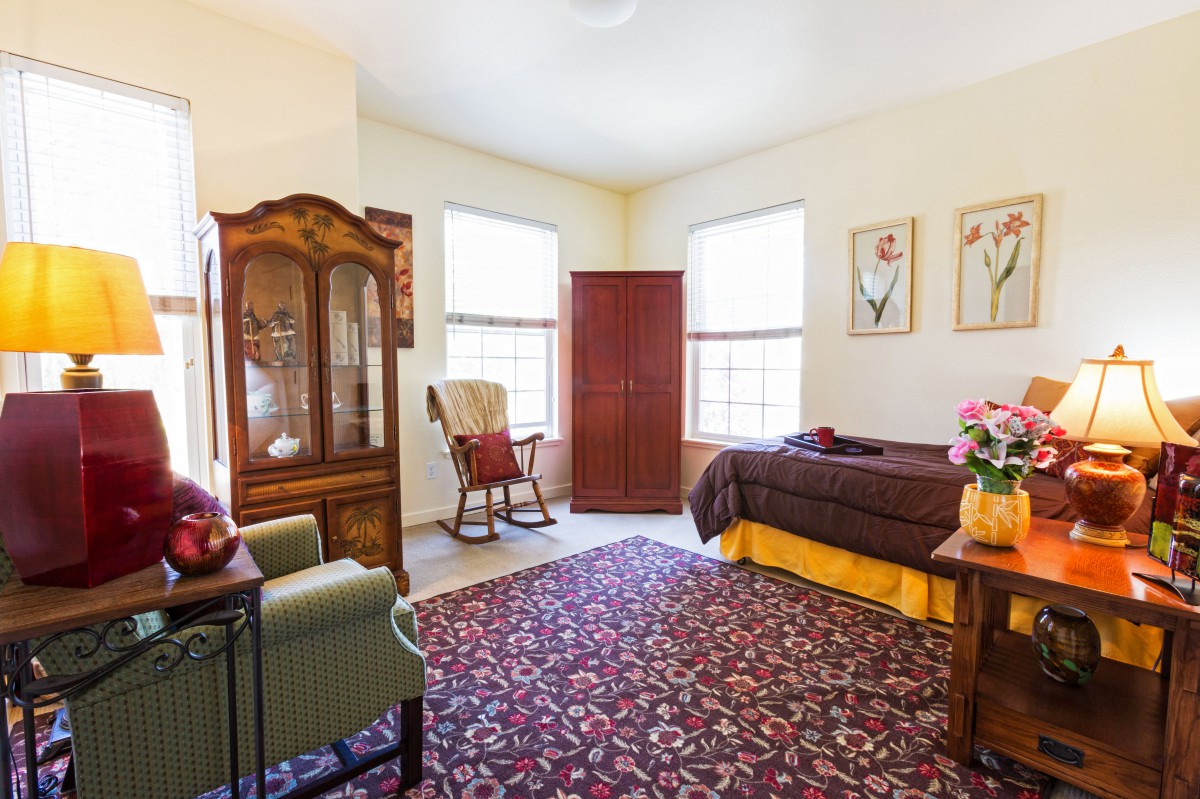 A cozy living room featuring a patterned carpet, rocking chair, and wooden cabinet with ample natural light.