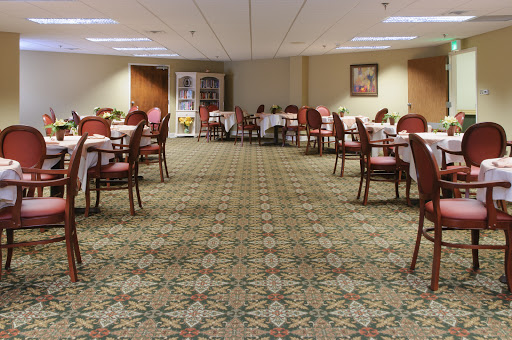 An elegant dining area featuring tables set with white tablecloths and comfortable chairs, adorned with a patterned carpet.