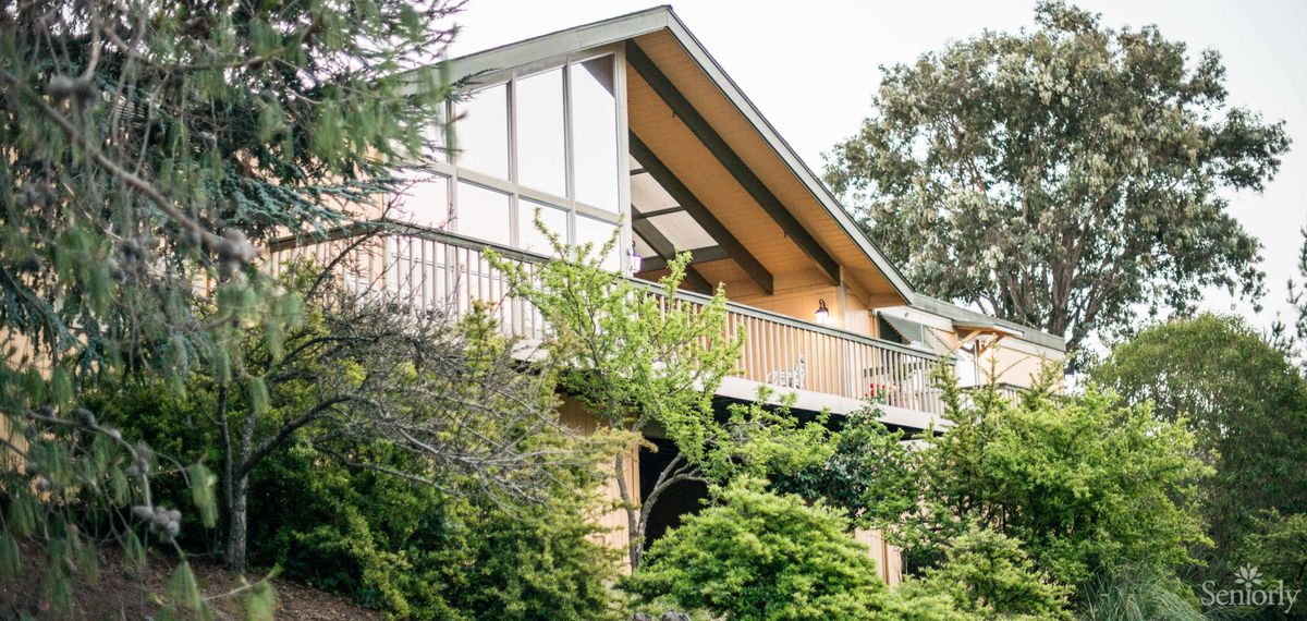 A modern house with a prominent balcony surrounded by lush greenery.