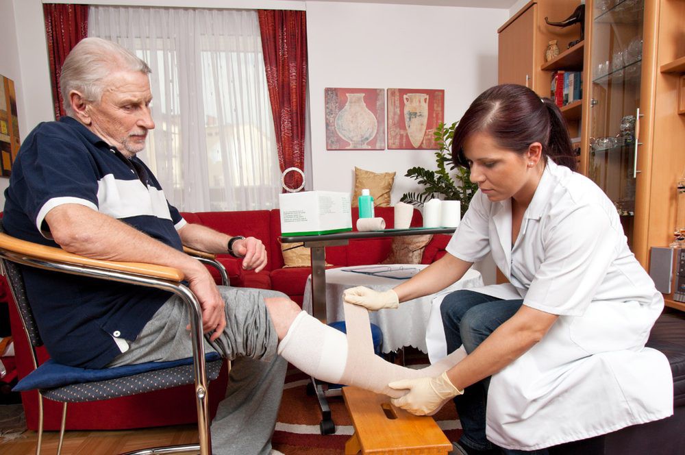 A nurse bandaging a patient's leg during a home visit.