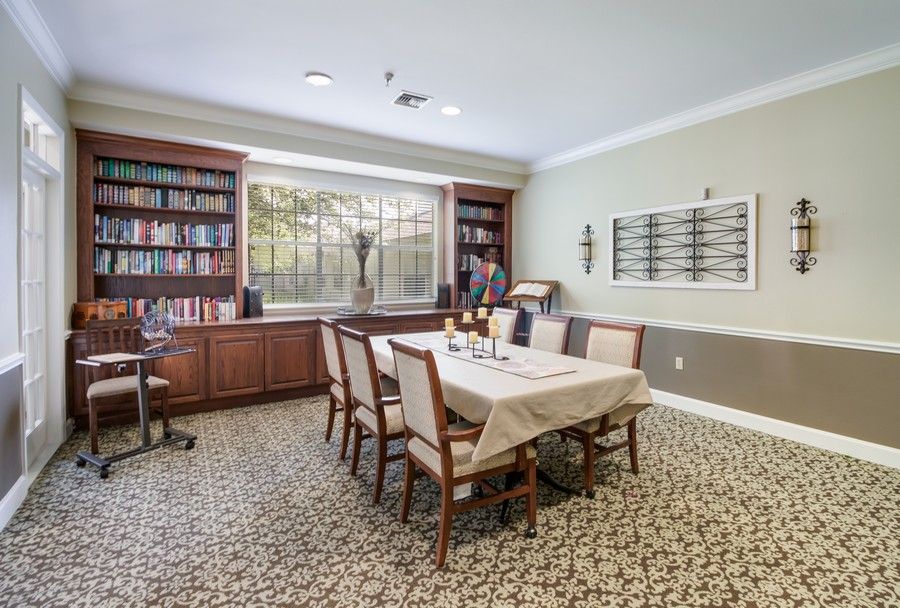 A cozy dining room with a table set for six, surrounded by bookshelves and a large window.