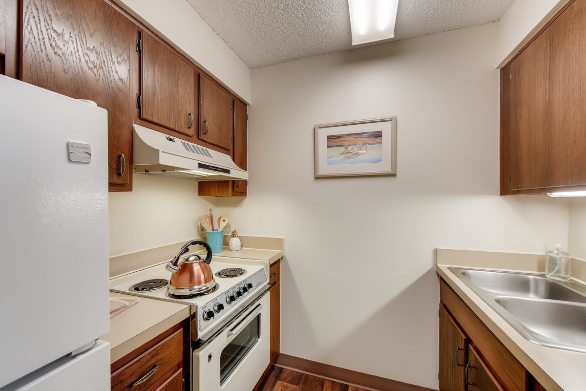 A compact kitchen with wooden cabinets, a stove, and a sink in an apartment.