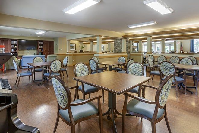 A spacious dining area with multiple tables and chairs, featuring a warm interior design and wooden flooring.