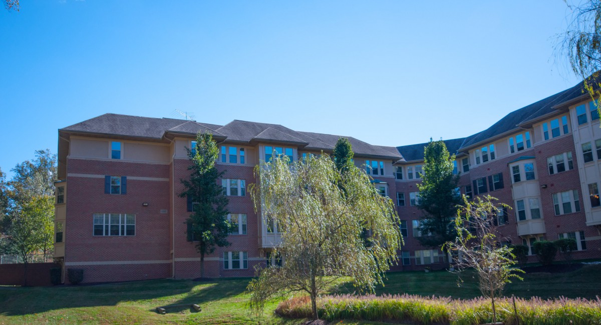 A brick building surrounded by trees and greenery under a clear blue sky.