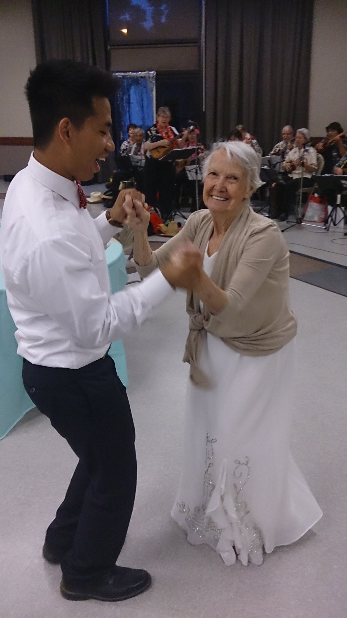 An elderly woman and a young man joyfully dancing together at an event.