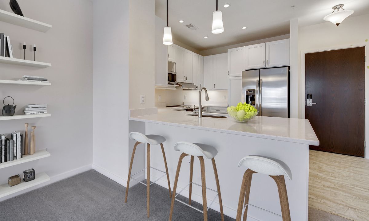 A modern minimalist kitchen with white cabinets, stainless steel appliances, and stylish bar stools.