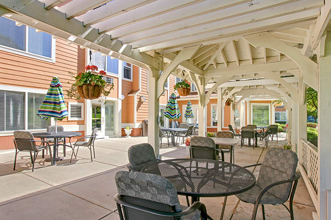 An outdoor patio with seating under a pergola, featuring hanging plants and tables with chairs.