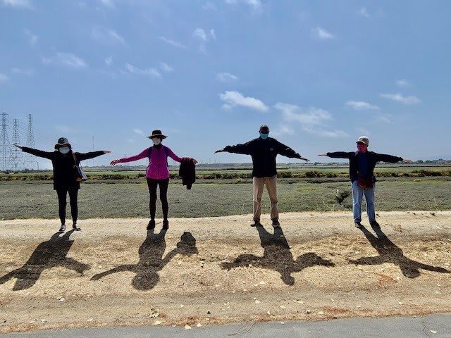 A group of people standing outdoors with their arms extended, casting shadows on the ground.