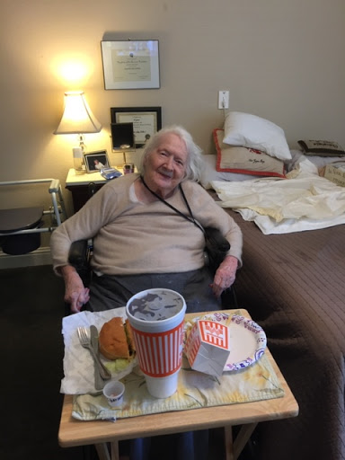 An elderly person enjoying a meal, smiling comfortably in their living space.
