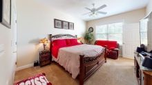 A cozy bedroom with a large bed featuring red accents and ample natural light.