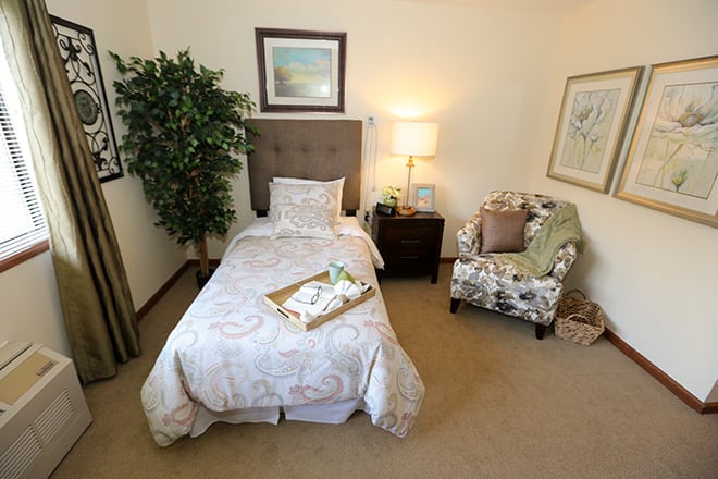 A cozy bedroom with a single bed, lamp, chair, and decorative elements.