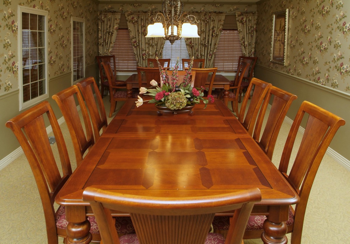 A well-decorated dining room with a wooden table and chairs, featuring a central floral arrangement and a chandelier overhead.