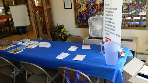 An indoor registration area featuring a blue table with papers, chairs, and a fan.
