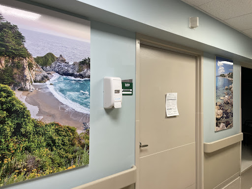 A serene beach landscape adorns the wall of a hospital corridor, providing calming decor in a healthcare setting.