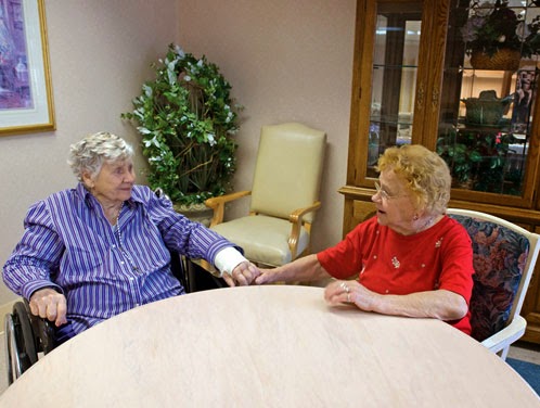 Two elderly women share a moment of connection and friendship in a care facility.