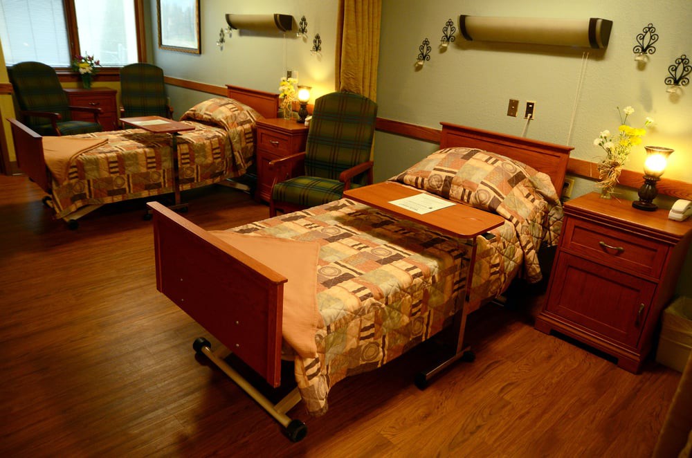 A hospital room with two patient beds and bedside tables.