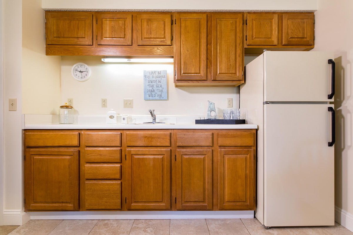 A kitchen with wooden cabinets, a refrigerator, and a clean countertop with a sink.