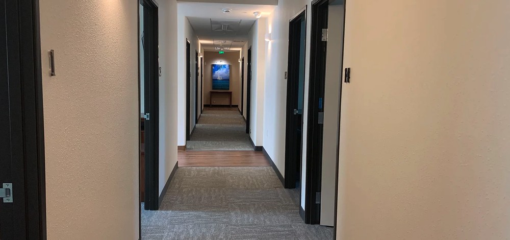 A long office hallway with multiple doors and carpeted flooring.