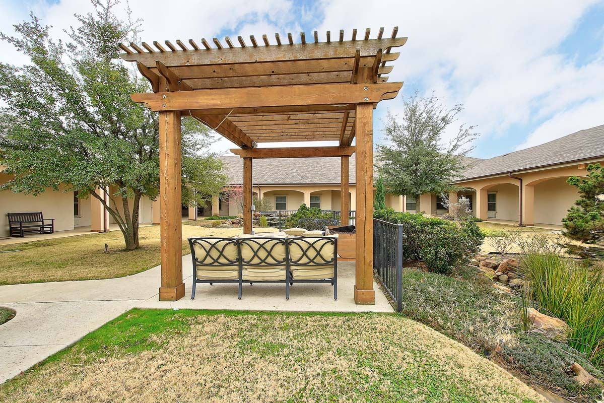 A wooden pergola with outdoor seating in a landscaped garden setting.