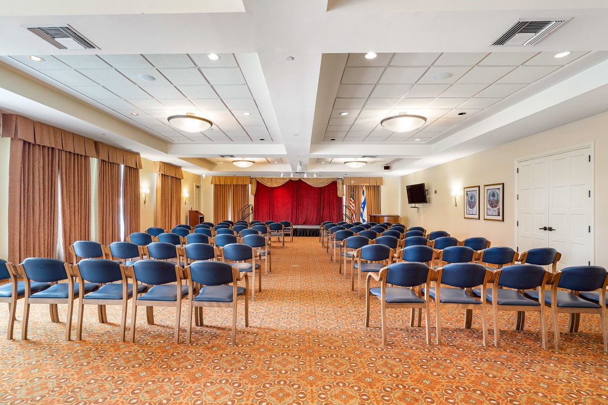 An empty conference room with rows of blue chairs facing a stage, ready for an event.
