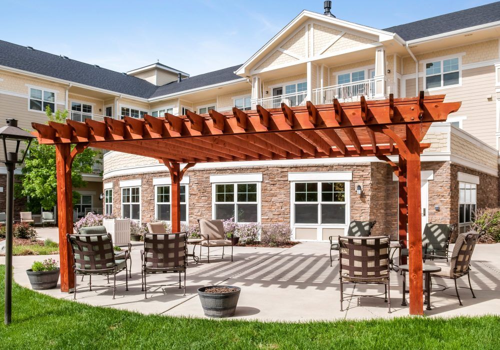 A sunny outdoor patio area with a pergola, surrounded by garden chairs and adjacent to a building.