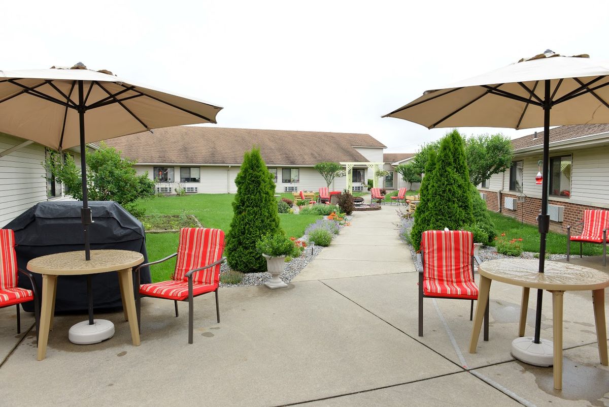 A well-maintained patio with red chairs, umbrellas, and lush greenery in a garden setting.