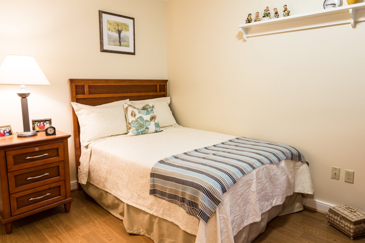 A cozy bedroom featuring a neatly made bed with decorative pillows and a striped blanket, complemented by wall art and a small shelf above.