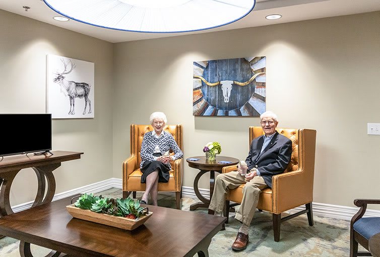 An elderly couple sitting in a modern living room adorned with artwork and decor.