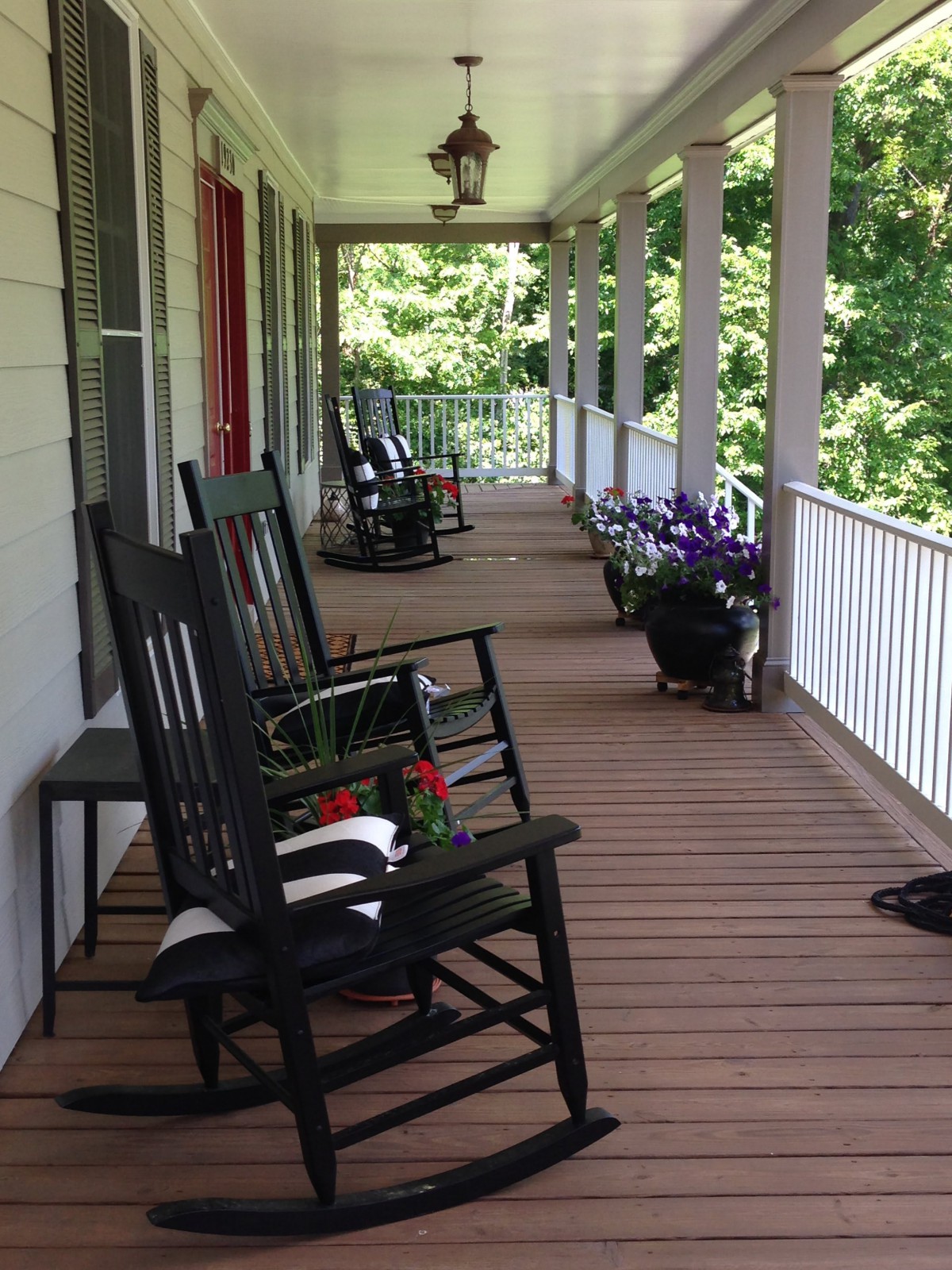 A cozy porch with black rocking chairs and potted plants along a wooden deck.