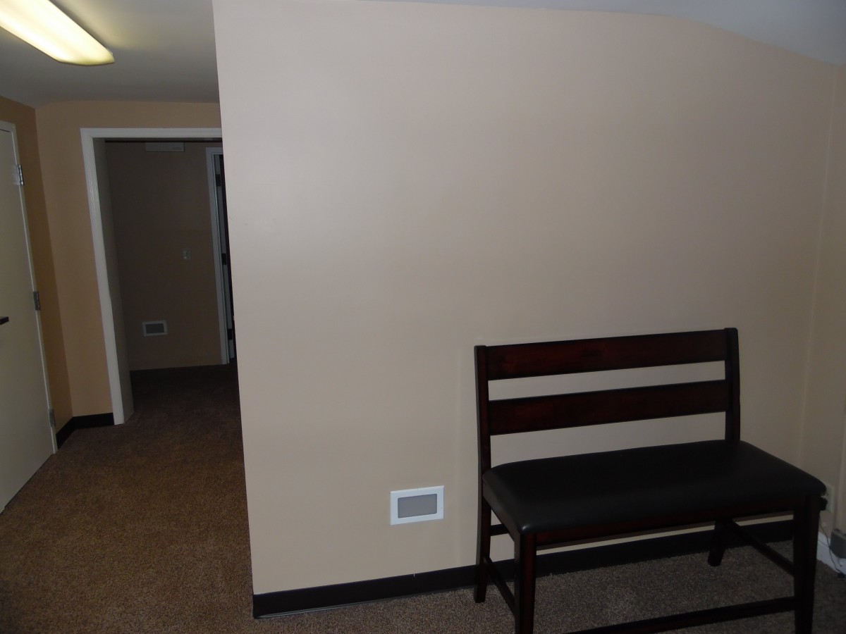 A simple interior featuring a wooden bench against a beige wall with a nearby hallway.