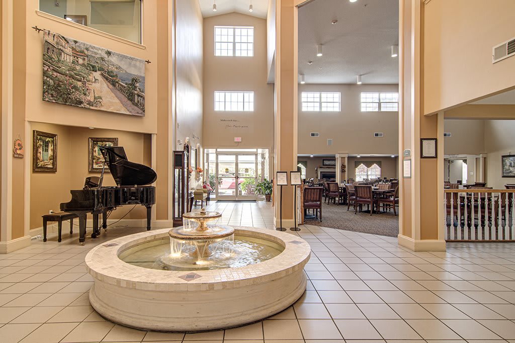 A spacious lobby featuring a central fountain and a grand piano with high ceilings and large windows.