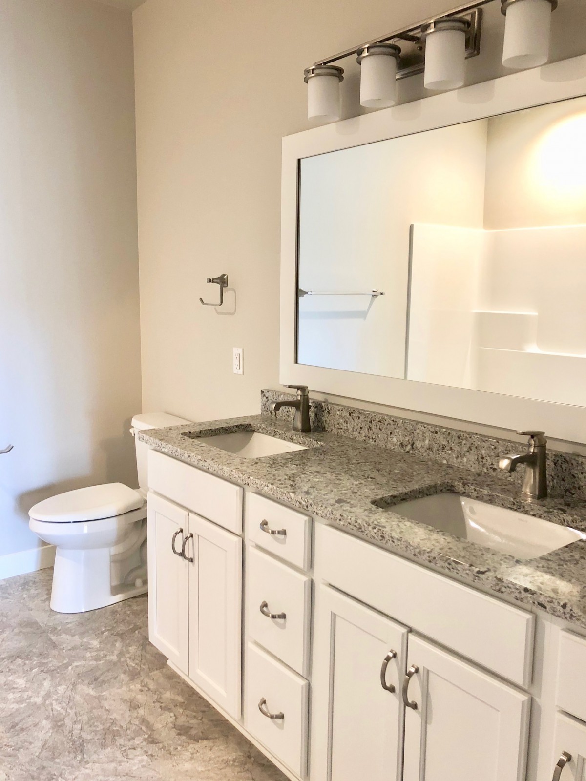 A modern bathroom featuring double sinks with granite countertops and white cabinetry.