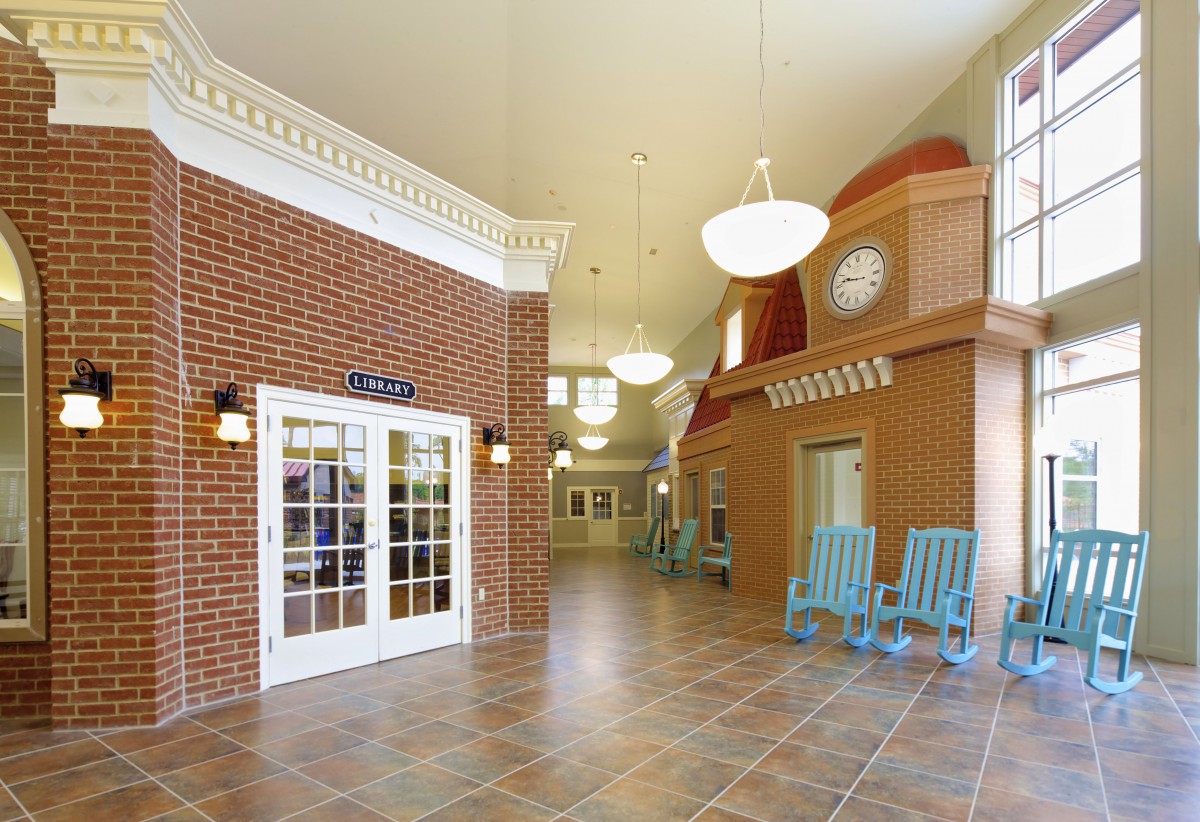 A spacious lobby area with brick walls, tile flooring, and blue rocking chairs.