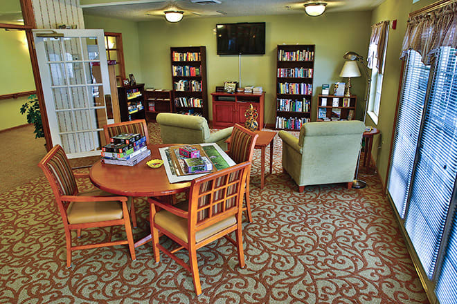 A cozy living room with comfortable seating, a television, and bookshelves filled with books. There is a table with puzzles in progress, creating a warm and inviting atmosphere.