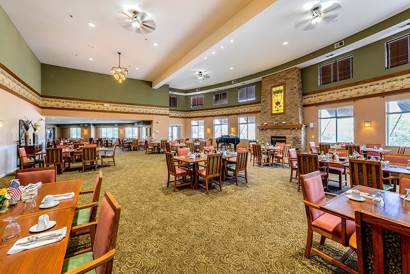 A spacious dining area with multiple tables and chairs, featuring a central fireplace and large windows.