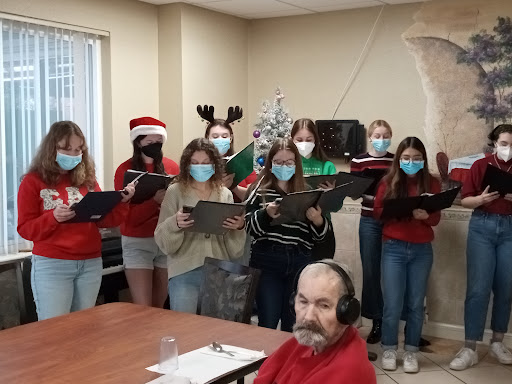 A cheerful group of holiday performers in festive attire singing together.