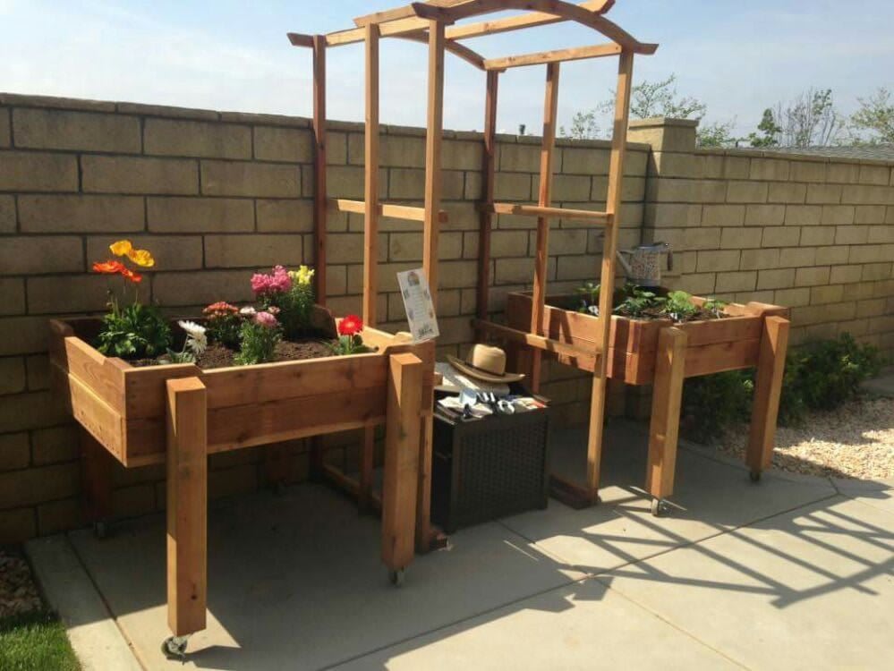 Raised wooden garden beds in a sunny backyard with flowers and a trellis.