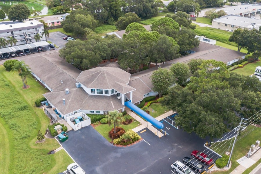 Aerial view of a building surrounded by trees with an adjacent parking lot.