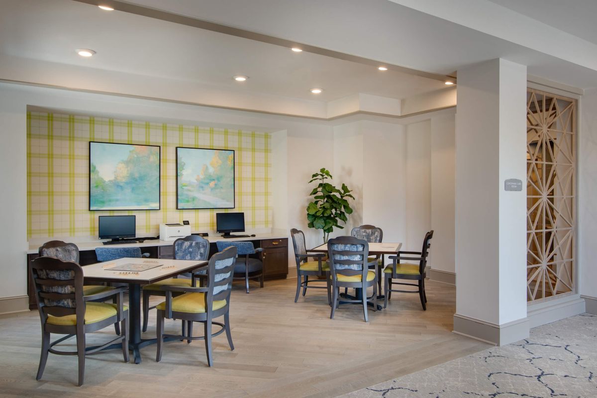 A modern office workspace featuring computers, tables, and chairs with artwork on the walls.