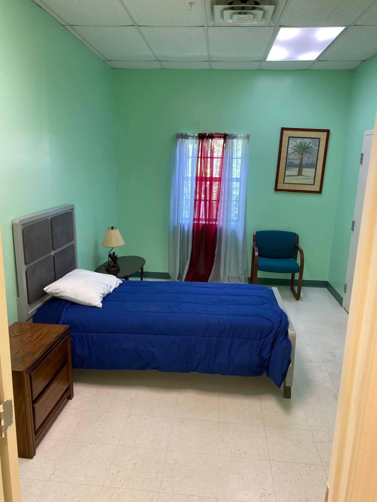 A small bedroom with a single bed, green walls, and blue bedding.