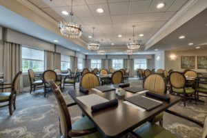 An elegant dining room with neatly arranged tables and chairs, adorned with chandeliers and large windows.