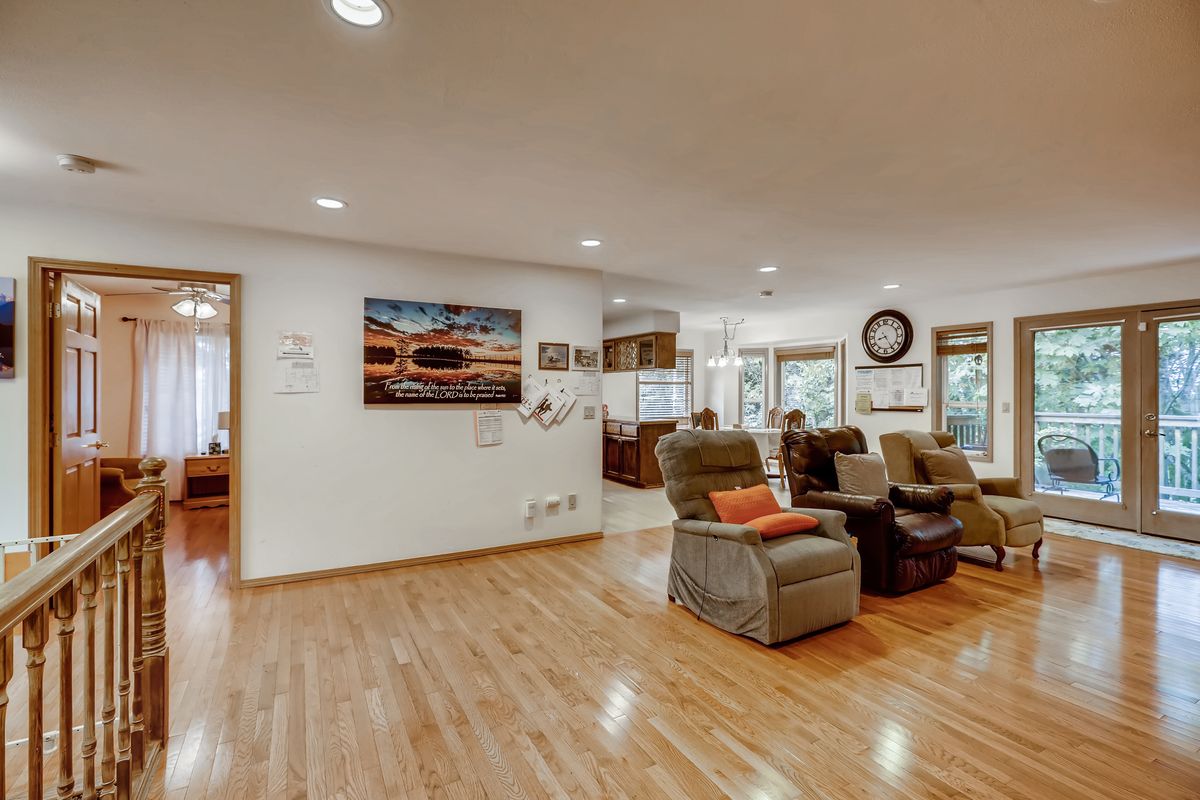A spacious living room with hardwood floors, featuring recliner chairs and artwork on the walls, illuminated by natural light.