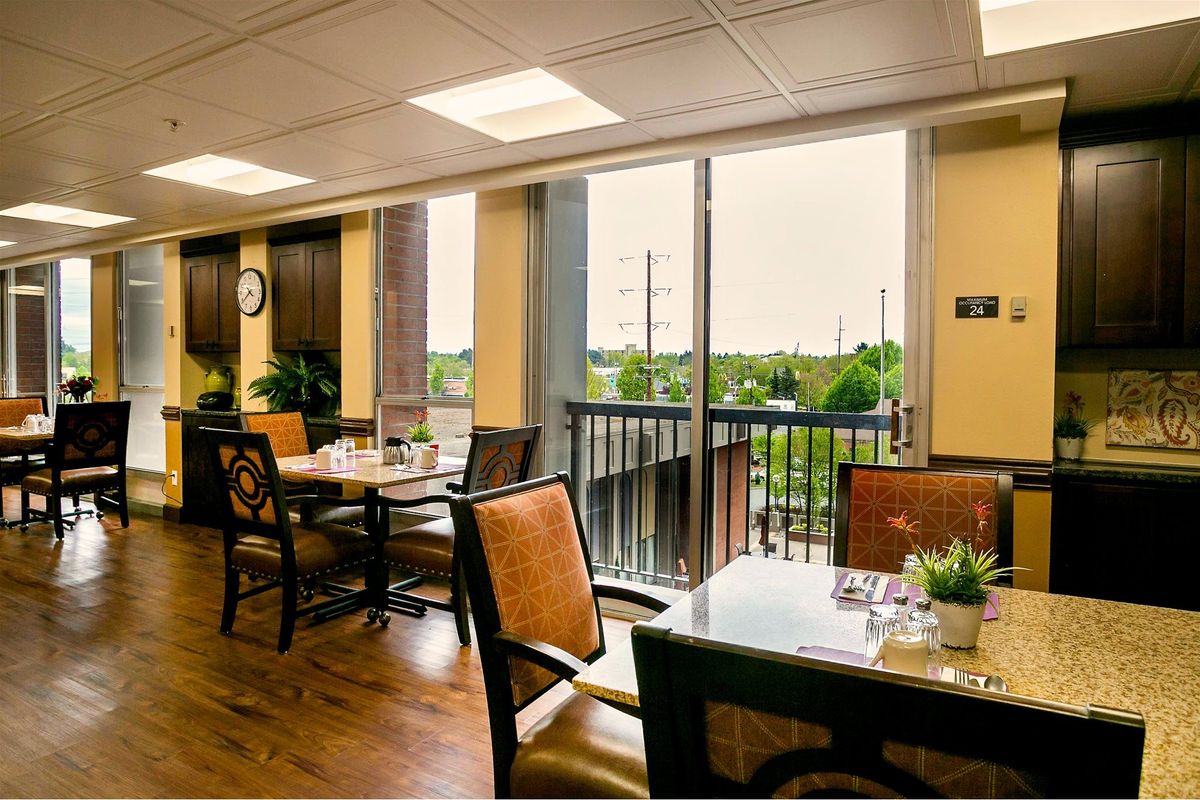 A cozy dining area with large windows, filled with natural light and decorated with plants.