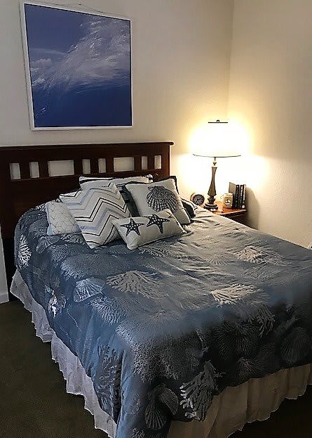 A cozy bedroom with a neatly made bed, decorative pillows, and a bedside lamp.