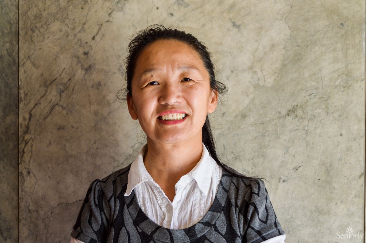 A woman smiling indoors against a textured wall.
