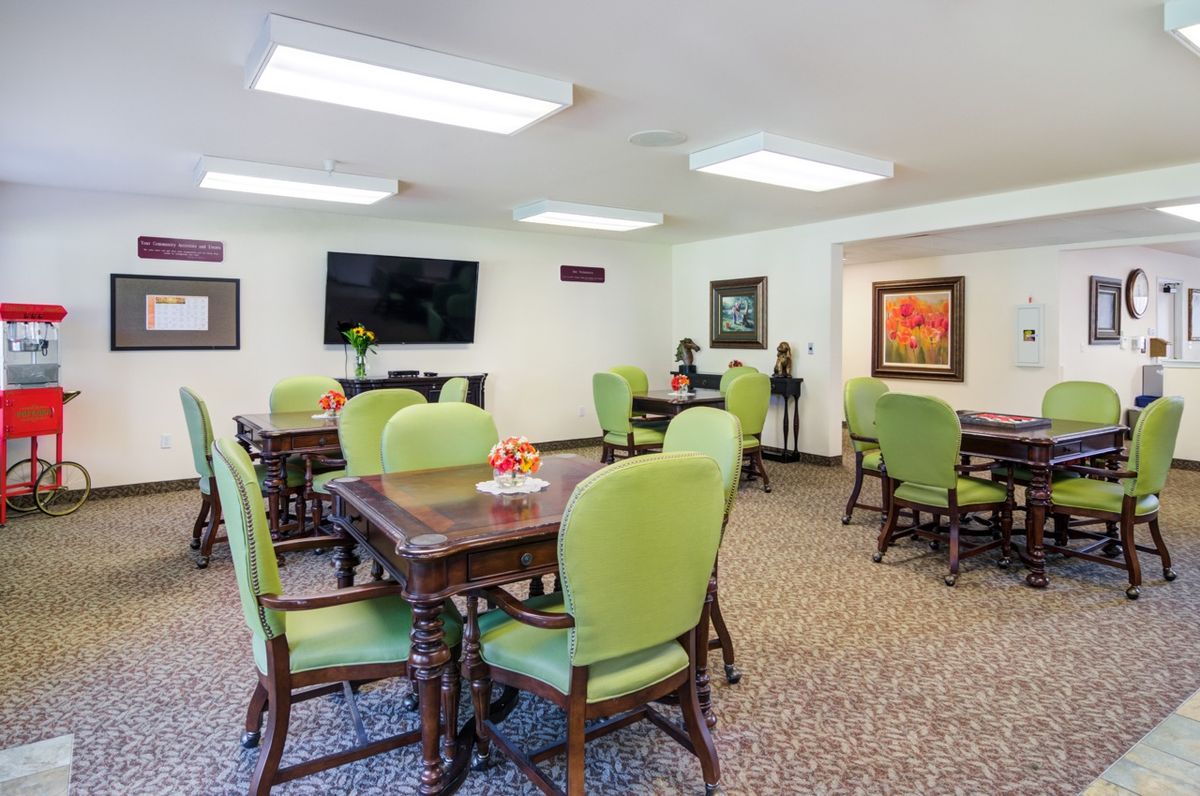 A well-lit dining area featuring green upholstered chairs, wooden tables, and a television on the wall.
