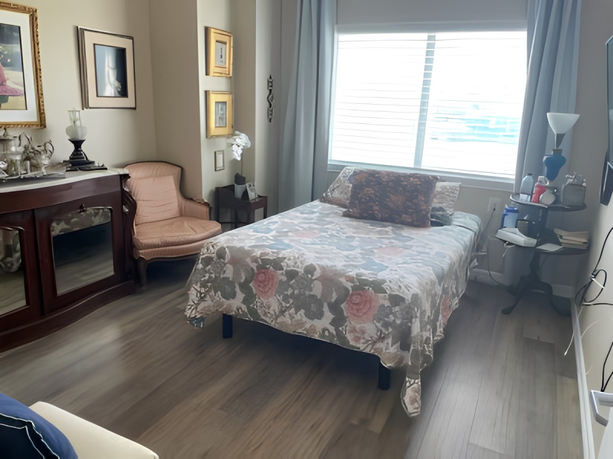 A cozy bedroom with a floral bedspread, chair, and desk by the window.